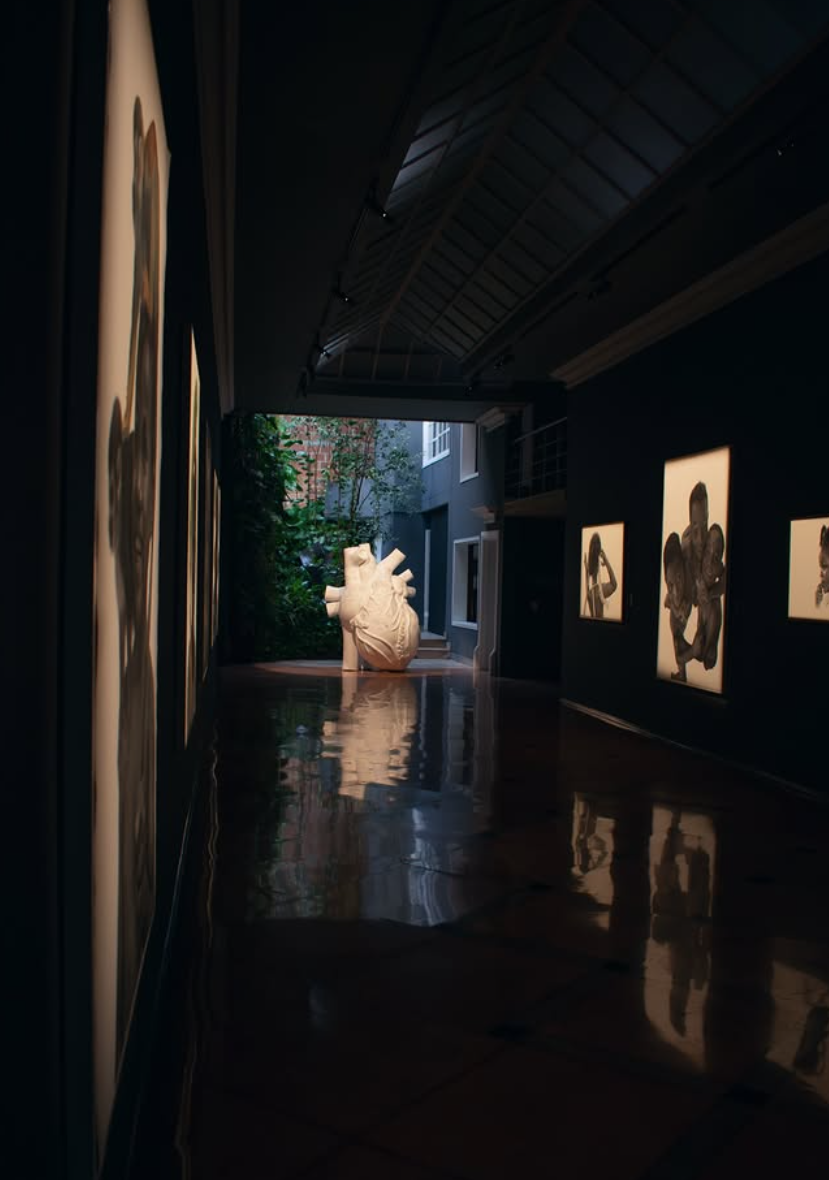 Espacio de exposición con obras en las paredes y un corazón blanco al fondo, junto a un patio